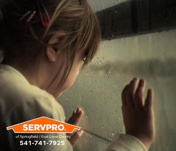 A child looks at the rain falling from a window.