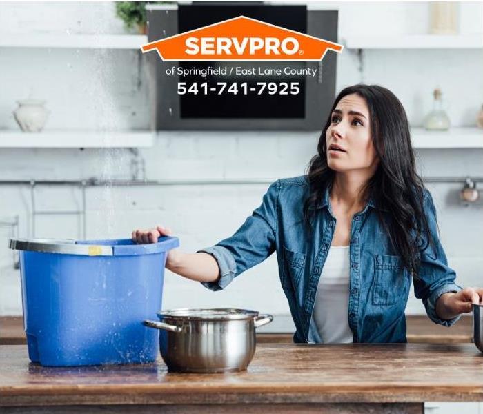 A woman uses pots and pans to capture water flowing into her kitchen from a leak in the ceiling.